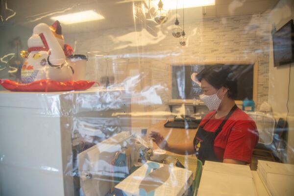 Jane Chung, owner of Family Baking, stands behind two clear shower curtains as she rings up a customer at her store inside the Atlanta Chinatown Shopping Mall in Chamblee, Friday, July 31, 2020. The clear curtains are used as a barrier to protect both employees and customers from transmitting germs while in the store. (ALYSSA POINTER / ALYSSA.POINTER@AJC.COM)