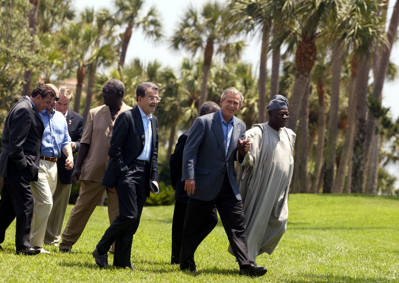 President Bush and Nigerian President Olusegun Obasanjo, far right, hold hands as South African President Thabo Mbeki, third right partially obscured, European Commission President Romano Prodi, center, Ghana's President John Kufuor, fourth from left, Russian President Vladimir Putin, second from left and German Chancellor Gerhard Schroeder, far left, walk together to pose for a group photo at the G-8 Summit in Sea Island, Ga., on Thursday June 10, 2004. Person third left is an unidentified protocol officer. (AP Photo/Laurent Rebours)