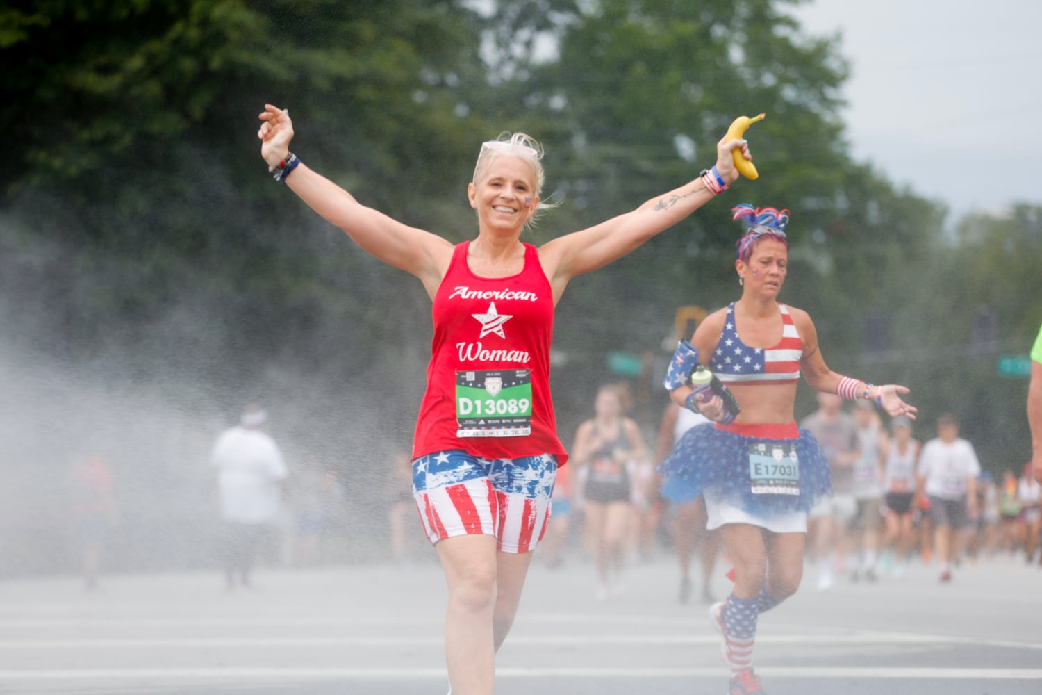 Runners cool off in the mist along Peachtree Street during the 54th running of the Atlanta Journal-Constitution Peachtree Road Race in Atlanta on Tuesday, July 4th, 2023.   (Natrice Miller / Natrice.Miller@ajc.com)