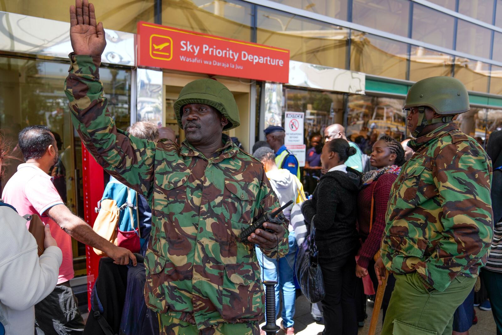 A Kenyan police officer gestures as stranded passengers wait for their delayed flights out of JKIA airport after flights were grounded following workers’ protesting a planned deal between the government and a foreign investor, in Nairobi, Kenya, Wednesday, Sept. 11, 2024. (AP Photo/Brian Inganga)