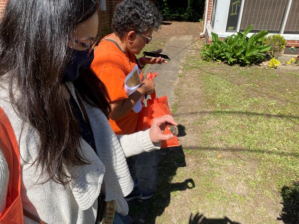 Eri Saikawa, an Emory researcher, left, examines a chunk of suspected lead slag in a west Atlanta neighborhood May 15, 2021. Resident Rosario Hernandez, right. ANDY MILLER / GEORGIA HEALTH NEWS