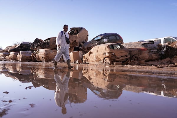 A man walks past stacked up cars after floods in Catarroja that left hundreds dead or missing in the Valencia region in Spain, Tuesday, Nov. 12, 2024. (AP Photo/Alberto Saiz)