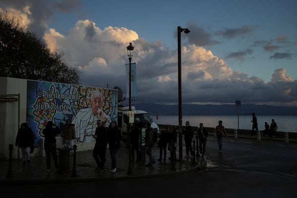 People walk past a mural featuring Pope Francis prior to the Pope's visit, in Ajaccio, in the southern French island of Corsica, Saturday, Dec. 14, 2024. (AP Photo/Thibault Camus)