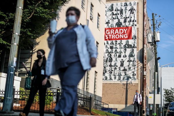 Medical workers arrive Tuesday, Aug. 10, at Grady Memorial Hospital against a large banner draped across the facade of a parking deck. COVID-19 cases are filling Georgia hospitals once again, igniting concerns of even more devastating outbreaks to come. (John Spink / John.Spink@ajc.com)

