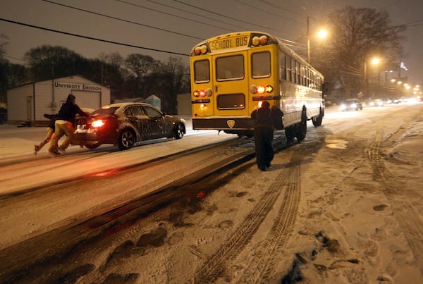 People push a car and attempt to push a school bus up an ice-covered University Avenue in Southwest Atlanta on Tuesday evening January 28, 2014 after a winter storm hit the Metro. BEN GRAY / BGRAY@AJC.COM