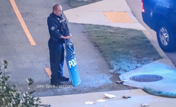 A Cobb police officer stands behind a ballistics shield and near a handgun outside the Walton on the Chattahoochee apartment complex on Akers Mill Road, where police were involved in a shooting with a suspect. JOHN SPINK / JSPINK@AJC.COM