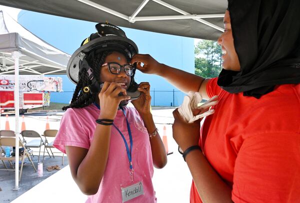 Kendall Eafford, 14, tries on an a helmet as Dianna Anthony, a firefighter with the City of Decatur, assists during a “Females in the Fire Service” event in Decatur. (Hyosub Shin / AJC)