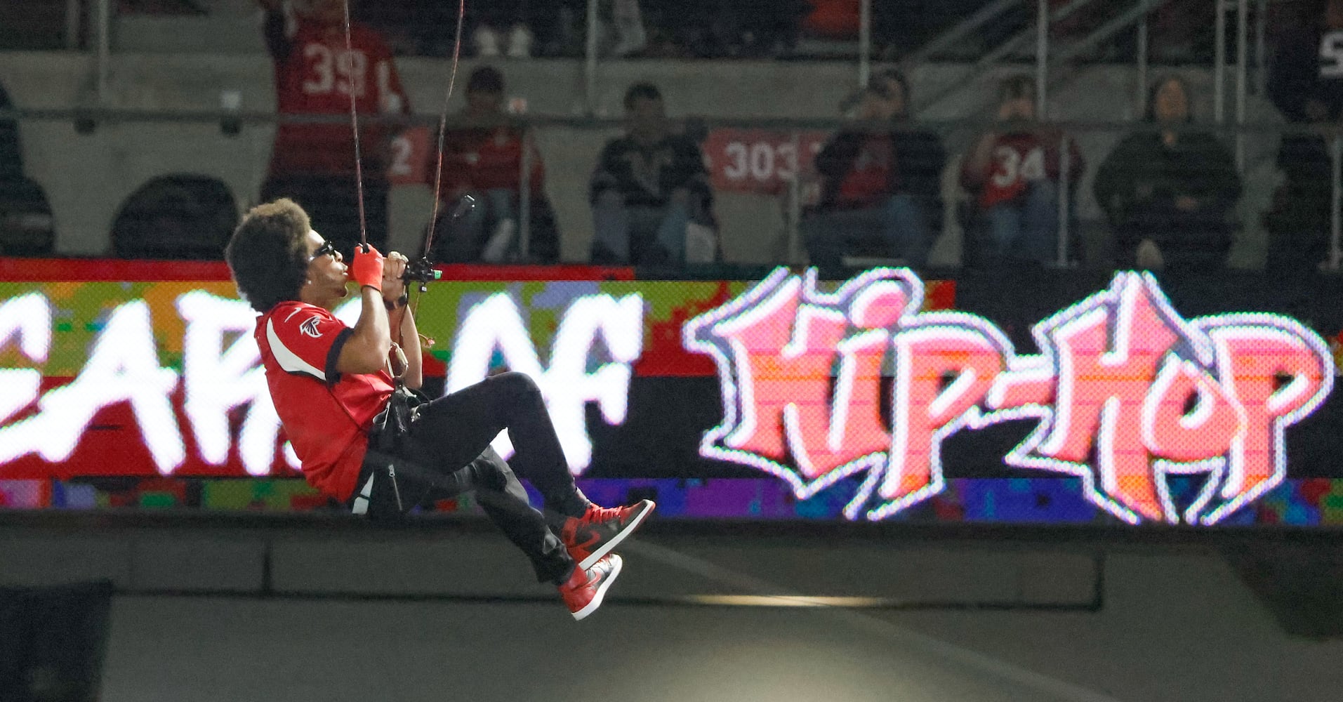 Ludacris descends from the top of the stadium while performing during the game.  The Atlanta Falcons celebrate Hip-Hop 50 with performances and appearances during their NFL football game between the Atlanta Falcons and the New Orleans Saints in Atlanta on Sunday, Nov. 26, 2023.   (Bob Andres for the Atlanta Journal Constitution)