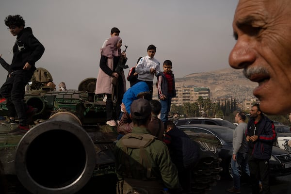 A youth, holding a rifle borrowed from a Syrian opposition fighter people, poses for a picture on the top of a government forces tank that was left on a street, at the Umayyad Square in Damascus, Syria, Wednesday, Dec. 11, 2024. (AP Photo/Leo Correa)