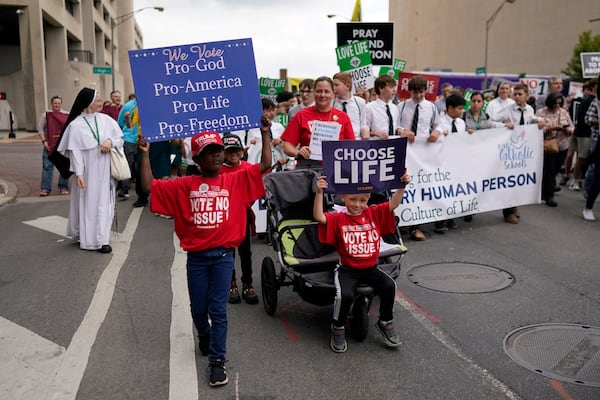 From left, Gianna Young, holding a sign that reads "We Vote Pro-God Pro-America Pro-Life Pro-Freedom" and her brothers Lucas and Isaac, holding a "Choose Life" sign, march with their mom, Erin Young, during the Ohio March for Life in Columbus, Ohio, Friday, Oct. 6, 2023. All three children are adopted. (AP Photo/Carolyn Kaster)