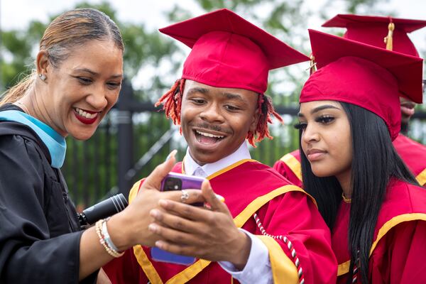 James Sims (center), a member of Creekside High School’s Tribe Academy, watches a video of himself from ninth grade before his graduation ceremony at Gateway Arena in College Park on Thursday, May 18, 2023. STEM teacher Demetrica Gorden is on his right. (Arvin Temkar / arvin.temkar@ajc.com)