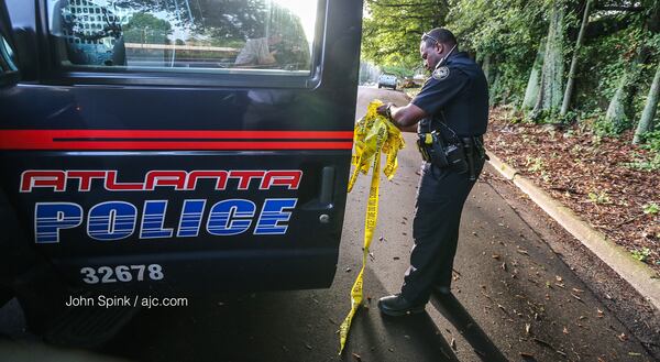 Atlanta police officer E. Irby picks up crime tape from Osborne Street where a deadly shooting occurred overnight. JOHN SPINK / JSPINK@AJC.COM