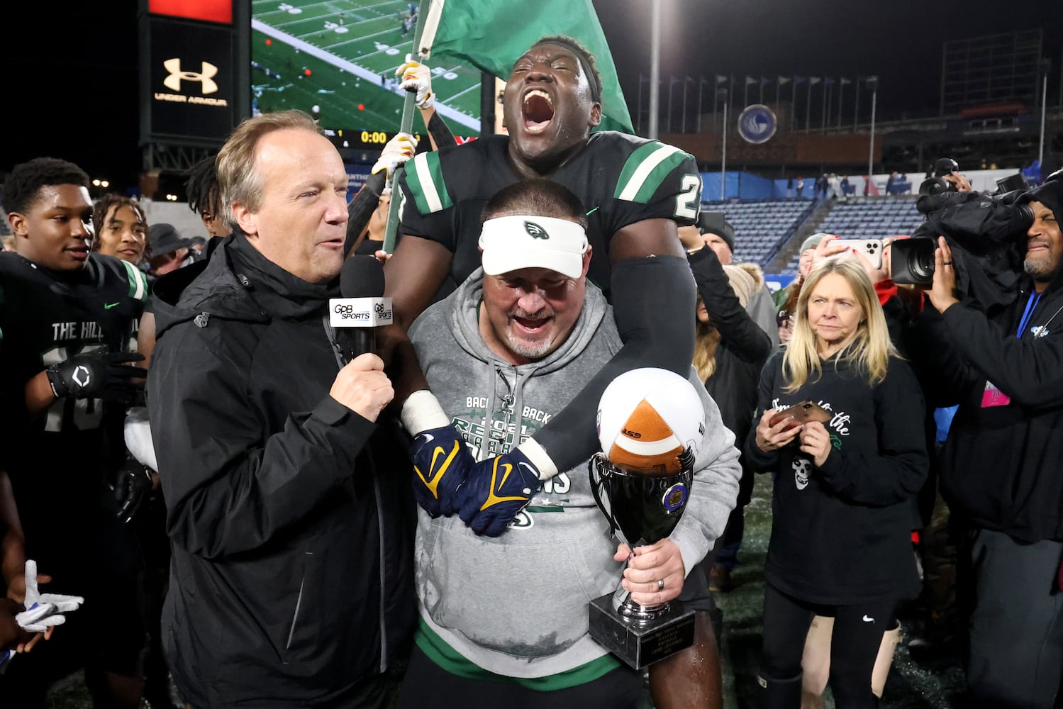 Collins Hill defensive lineman Asani Redwood (23) jumps on the back of head coach Lenny Gregory as Gregory is interviewed after their 24-8 win against Milton in the Class 7A state title football game at Georgia State Center Parc Stadium Saturday, December 11, 2021, Atlanta. JASON GETZ FOR THE ATLANTA JOURNAL-CONSTITUTION