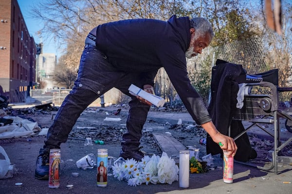 Lucky Hollins places candles Friday at the site of an encampment where an unhoused man was killed in a city cleanup operation the day before. Ben Hendren/AJC