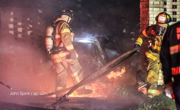 DeKalb County firefighters battled flames that engulfed two cars and a brick house early Monday on Raleigh Drive. JOHN SPINK / JSPINK@AJC.COM