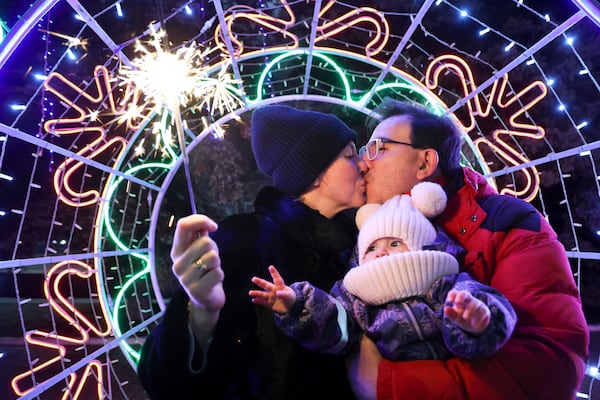 A couple share a tender moment as they walk with their child in a square decorated for Christmas and the New Year festivities in Donetsk in Russian-controlled Donetsk region, eastern Ukraine, Tuesday, Dec. 31, 2024. (AP Photo/Alexei Alexandrov)