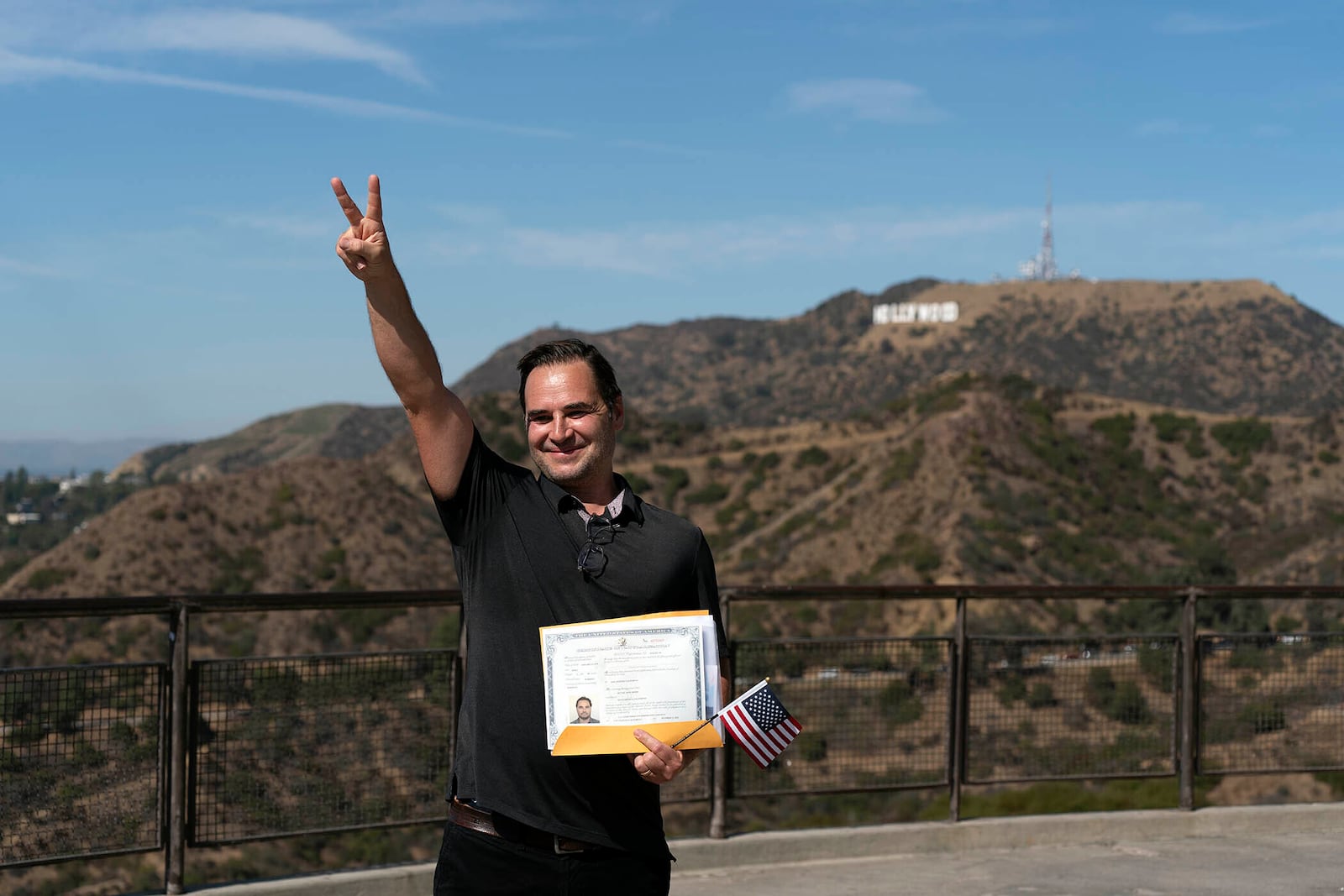 Dennis Beier, a 46-year-old film producer from Germany, flashes a sign while posing for photos with the Hollywood sign following a naturalization ceremony at Griffith Observatory in Los Angeles, Monday, Oct. 21, 2024. (AP Photo/Jae C. Hong)