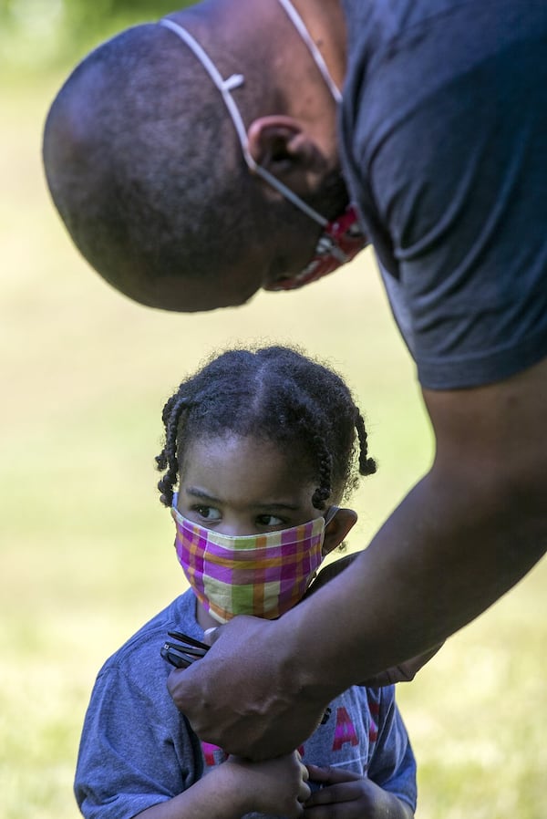 Parker Hughes gets her face mask adjusted by her father, Todd Hughes, as she plays in an open field following a pull-up portrait session with photographer Melissa Alexander in Atlanta's West End community, Friday, May 1, 2020. The family has not been out much since the shelter-in-place order was placed on Georgia citizens. ALYSSA POINTER/ALYSSA.POINTER@AJC.COM