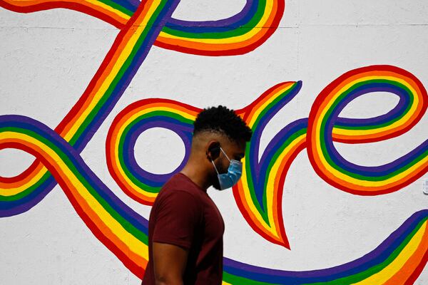 A mural covers a boarded-up window as a man wearing a face mask to protect against the spread of the new coronavirus walks by, Sunday, June 7, 2020, in Washington, the morning after massive protests over the death of George Floyd, who died after being restrained by Minneapolis police officers. (AP Photo/Patrick Semansky)