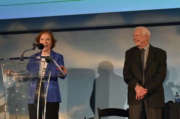 Jimmy Carter looks on in delight as his wife, Rosalynn, addresses the audience at the Bill Foege Global Health Awards ceremony held at the Delta Flight Museum. The 90-year-old former first lady recently underwent surgery but said she "had" to come speak about Foege and the award's sponsor, MAP International. Hyosub Shin/AJC