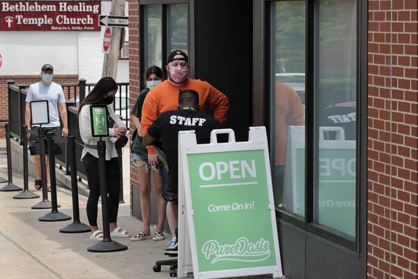 In this Wednesday, June 24, 2020, photograph, customers wait in line at Pure Oasis, a Black-owned recreational marijuana dispensary, in the Grove Hall neighborhood of Boston. Many from outside Boston have recently shopped and supported the store which was robbed and vandalized earlier in the month.