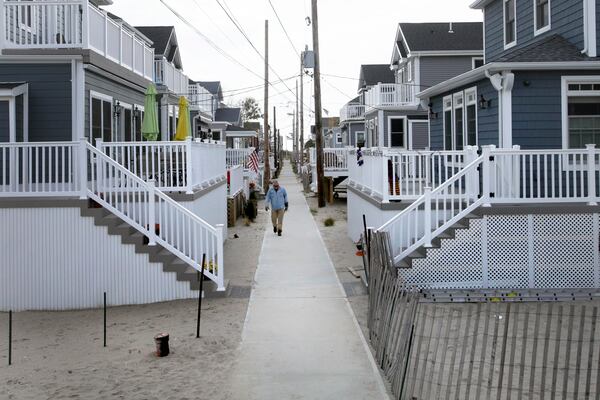 In this Oct. 15, 2014 photo, a man walks on a sidewalk in the Breezy Point neighborhood in the Queens borough of New York. Two years ago a fire raged across this oceanfront community during Superstorm Sandy, destroying 130 homes, including those that lined this walk. The new houses are all built on elevated concrete foundations to protect them from future storms. (AP Photo/Mark Lennihan)