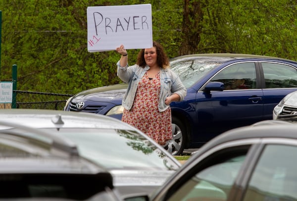 Summer Osbon holds up a sign as her father, Pastor Shell Osbon, talks to the crowd during the Drive-in church service at the Life Church Smyrna Assembly of God Sunday, April 5, 2020 STEVE SCHAEFER / SPECIAL TO THE AJC