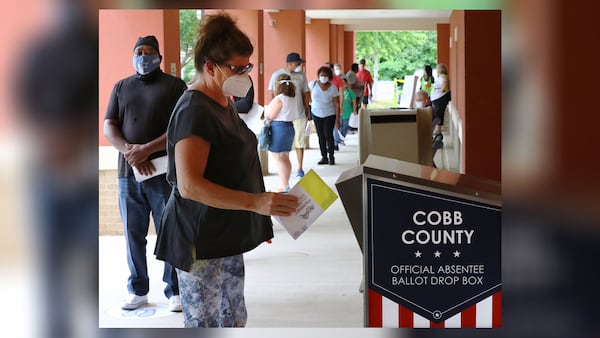 Nina Wilson drops off her absentee ballot while dozens of other voters line up to cast their votes in person on the first day of early voting at the Cobb County Board of Elections & Registration on Monday, May 18, 2020, in Marietta.   Curtis Compton ccompton@ajc.com