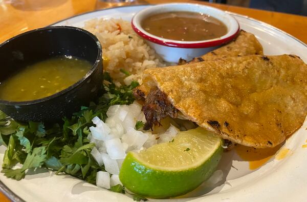 Birria tacos from Antiguo Lobo are a flavor sensation featuring juicy braised brisket inside corn tortillas that have been dipped in meaty consommé then griddled. For a full meal, order the birria plate that brings two tacos, rice and Mexican charro beans. (Ligaya Figueras / ligaya.figueras@ajc.com)