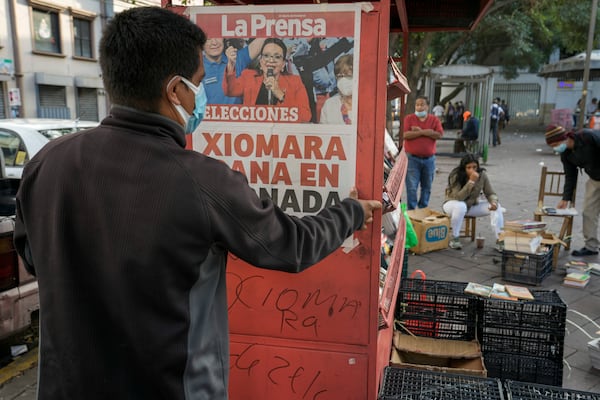 FILE - A man hangS a poster with a photo of presidential candidate Xiomara Castro and the day's headline of her expected victory at his newspaper stand after general elections in Tegucigalpa, Honduras, Nov. 29, 2021. (AP Photo/Moises Castillo, File)