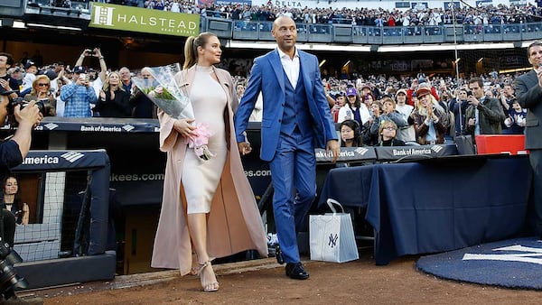 Derek Jeter and wife Hannah walk from the dugout to the field during a pregame ceremony retiring Jeter's number 2 in Monument Park at Yankee Stadium Sunday.