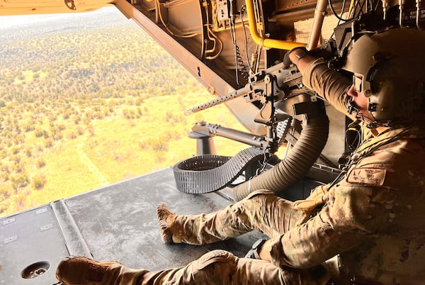 Osprey flight engineer Tech Sgt. Brett McGee sits on the back open ramp of the V-22 and holds the aircraft's .50 caliber gun as the crew flies over a New Mexico training range Oct. 9, 2024, near Cannon Air Force Base. (AP Photo/Tara Copp)