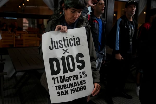 A fan of the late soccer star Diego Maradona holds a sign that reads in Spanish "Justice for God" outside the court where members of the medical team that treated Maradona go on trial for alleged homicide by negligence in San Isidro on the outskirts of Buenos Aires, Argentina, Tuesday, March 11, 2025. (AP Photo/Natacha Pisarenko)