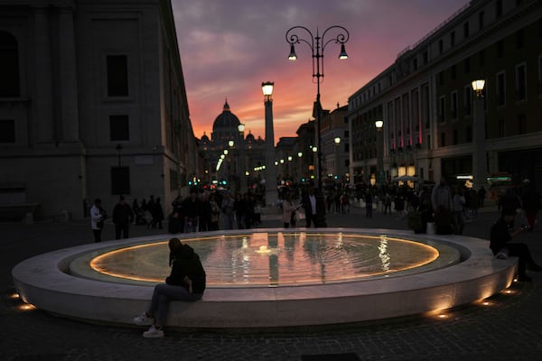 Locals and tourists walk along a main street near St. Peter's Basilica, background, as the sun sets in Rome, Italy, Friday, March 7, 2025. (AP Photo/Francisco Seco)