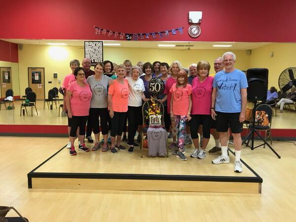 Marcia Sasser, third from the right in the front row, was a regular attendee at SilverSneakers classes in Marietta. The group became more like family, she previously told the AJC. Here, they celebrate their trainer's 50th birthday with T-Shirts and balloons. In early August, Sasser died due to COVID-19. CONTRIBUTED