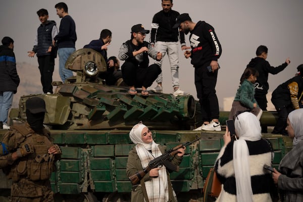 A woman holding a rifle borrowed from a Syrian opposition fighter poses for a picture, next to a government forces tank that was left on a street, at the Umayyad Square in Damascus, Syria, Wednesday, Dec. 11, 2024. (AP Photo/Leo Correa)