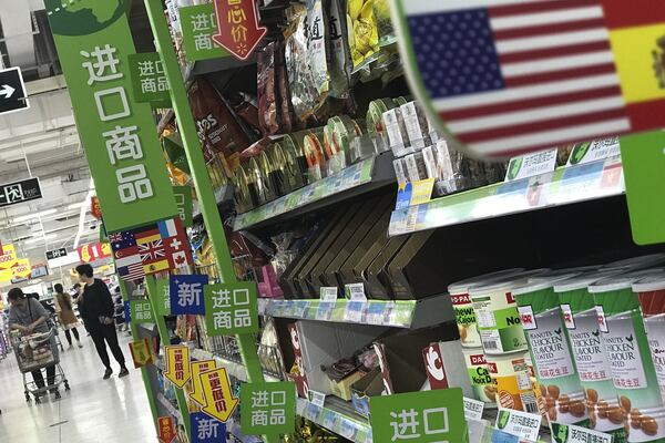 Women push a shopping cart near nuts and sweets imported from the United States and other countries displayed on a section selling imported foods at a supermarket in Beijing, Monday, April 2, 2018. China raised import duties on a $3 billion list of U.S. pork, fruit and other products Monday in an escalating tariff dispute with President Donald Trump that companies worry might depress global commerce. (AP Photo/Andy Wong)