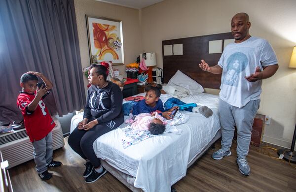 The White family lives in an extended-stay hotel on Wednesday, Dec 21, 2022.  King, 7, checks his new hair cut with his mother Raneice as Mckenzie, 10, watches over her 5-month-old sister Justice and 4-year-old Legend sleeps.  The family has lived in extended-stay hotels for years.  Despite Melvin, standing right, working full-time, they canÕt find long-term safe housing they can afford.  (Jenni Girtman for The Atlanta Journal-Constitution)