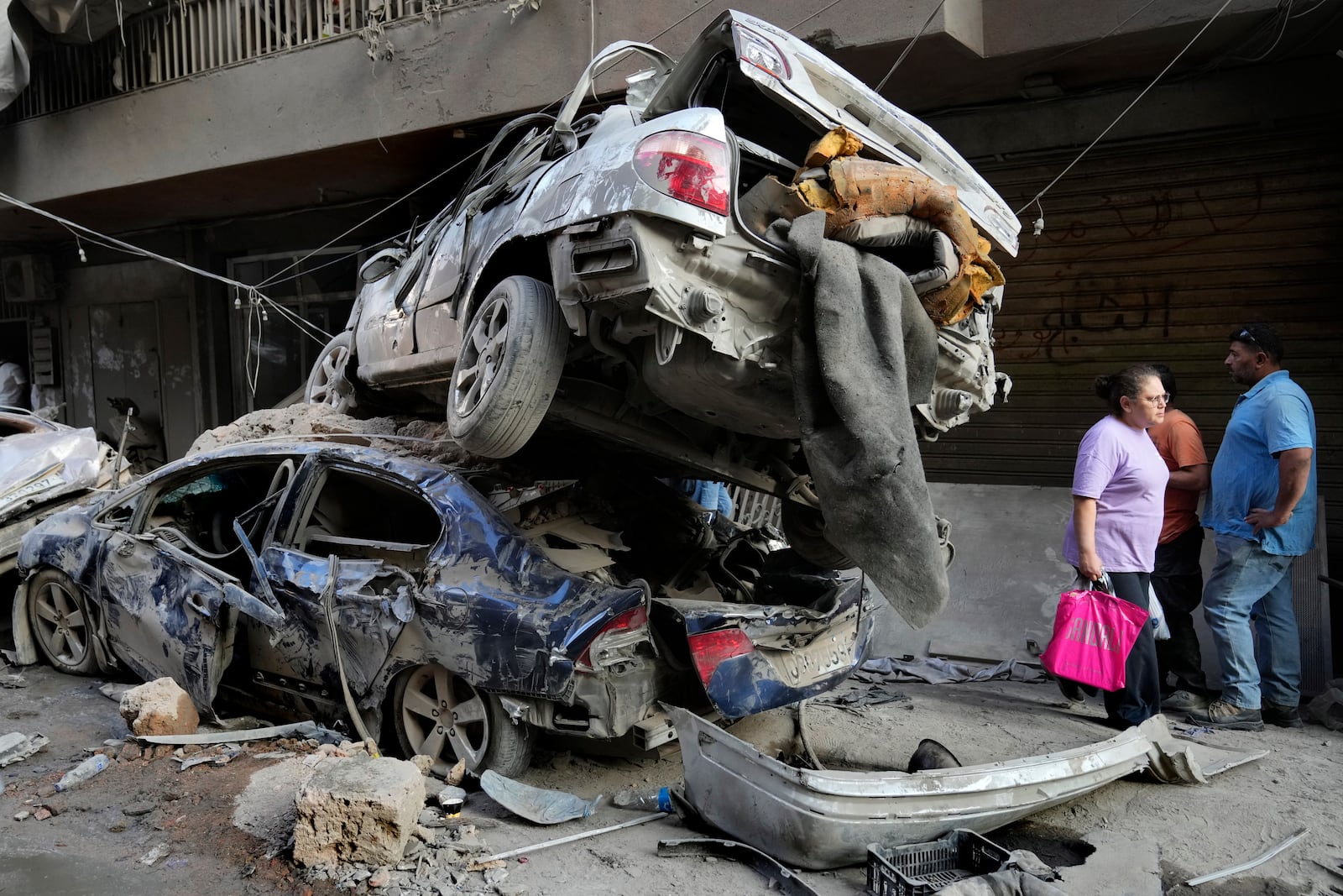 A Lebanese woman passes next of destroyed cars at the site of Thursday's Israeli airstrike, in Beirut, Lebanon, Friday, Oct. 11, 2024. (AP Photo/Hussein Malla)