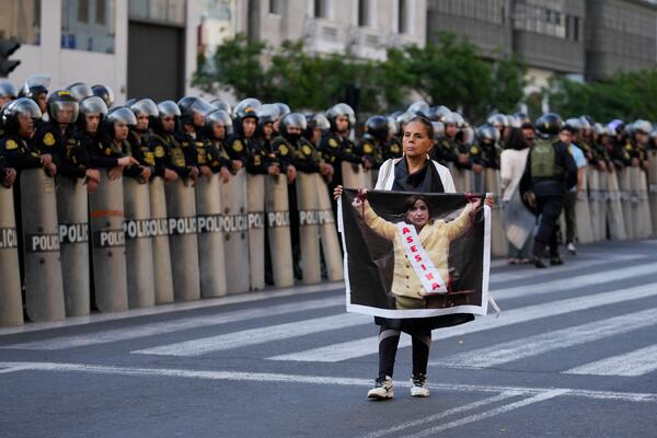 An anti-government protester holds a photo of Peru's President Dina Boluarte with a sash that reads in Spanish, "Assassin" during a demonstration on the sidelines of the Asia-Pacific Economic Cooperation (APEC) summit in Lima, Peru, Wednesday, Nov. 13, 2024. (AP Photo/Fernando Vergara)