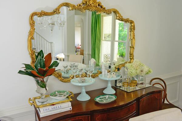 Milk glass, coffee table books, and a mirrored tray create a tableau beneath the a baroque-style gilded mirror Edee found at an antique store.