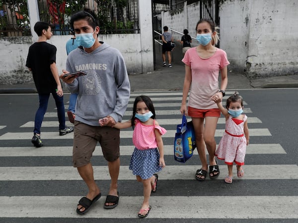 A family wearing protective masks crosses a street in the Philippines. The Philippines on Sunday reported the first death of a new virus outside of China.