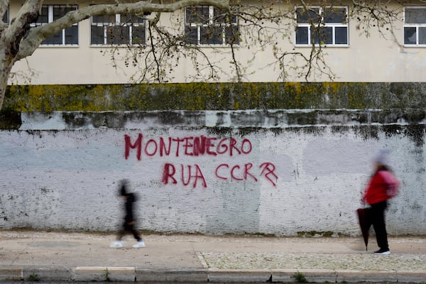 People walk past a graffiti saying "Montenegro Out", referring to Portuguese Prime Minister Luis Montenegro, the day before his government faces a confidence vote in parliament, in Lisbon, Monday, March 10, 2025. (AP Photo/Armando Franca)