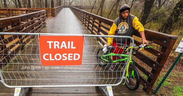 Edwin Lester backs out of riding on the Noonday Creek Bridge in Woodstock on Thursday after officials closed the trail due to flooding. JOHN SPINK / JSPINK@AJC.COM