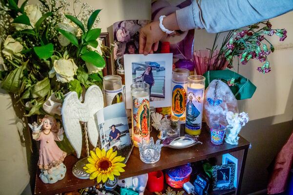 Jessica Aguilar holds up a photograph of her mother from a memorial altar in their Roswell dining room Sunday, January 23, 2022. Besides stills from her mother's life, the altar also held religious candles, and some of her mother's personal belongings, like a hair brush. STEVE SCHAEFER FOR THE ATLANTA JOURNAL-CONSTITUTION