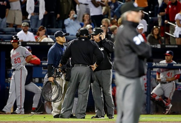 Umpires listen to headsets as a play is under review in the seventh inning of a baseball game between the Atlanta Braves and the Washington Nationals, Friday, April 11, 2014, in Atlanta. (AP Photo/David Goldman) There was a lot of standing around Friday. (David Goldman/AP)