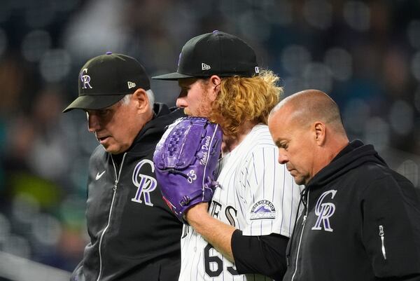 FILE - Colorado Rockies relif pitcher Noah Davis, center, is escorted from the mound by manager Bud Black, back, and assistant trainer Heath Townsend after suffering an injury in the seventh inning in the second baseball game of a doubleheader against the Seattle Mariners, Sunday, April 21, 2024, in Denver. (AP Photo/David Zalubowski, File)