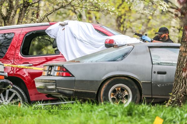 Authorities on the scene have a white sheet covering an area where two cars are parked in the driveway. JOHN SPINK / JSPINK@AJC.COM