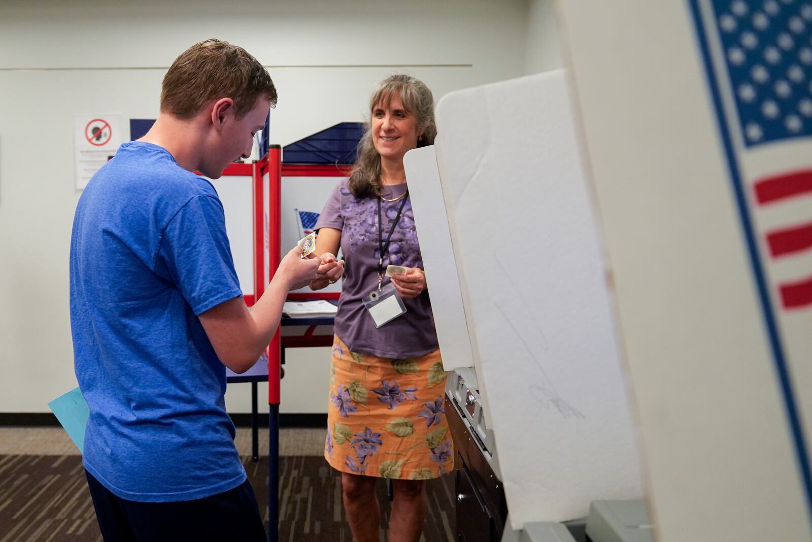 An election worker hands first-time voter Ethan Stregack, 18, left, a sticker after he cast his ballot, Thursday, Oct. 31, 2024, in Falls Church, Va. (AP Photo/Stephanie Scarbrough)