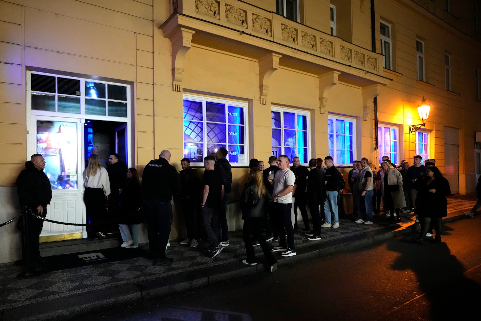 A group of tourists stand in line outside a bar as they attend a pub crawl tour in downtown Prague, Czech Republic, Thursday, Oct. 17, 2024. (AP Photo/Petr David Josek)